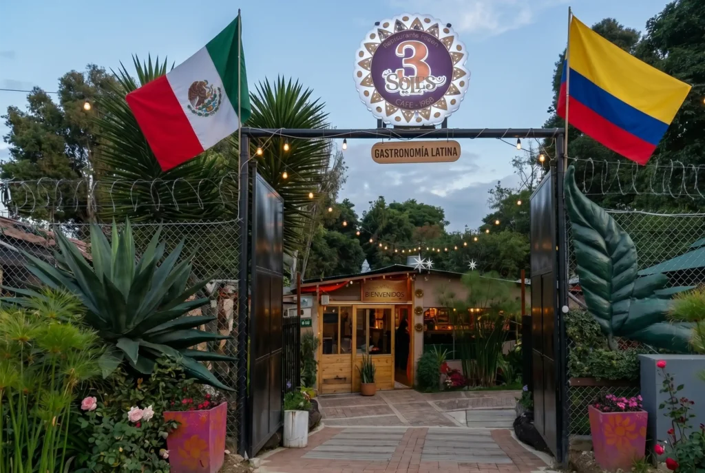 Entrada principal del Restaurante 3 Soles con banderas de México y Colombia, letrero luminoso y jardín exterior.