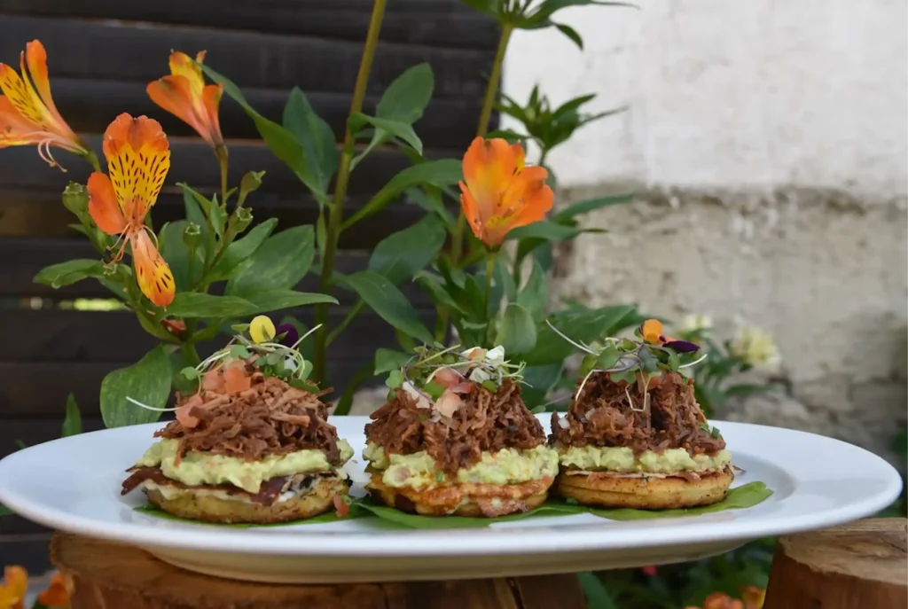 Tres arepas gourmet de maíz rellenas de ropa vieja, guacamole y brotes frescos, presentadas de forma artística en el Restaurante 3 Soles.