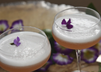 Dos copas de Pisco Sour con espuma cremosa y flores púrpuras comestibles, servidos en la barra del Restaurante 3 Soles.