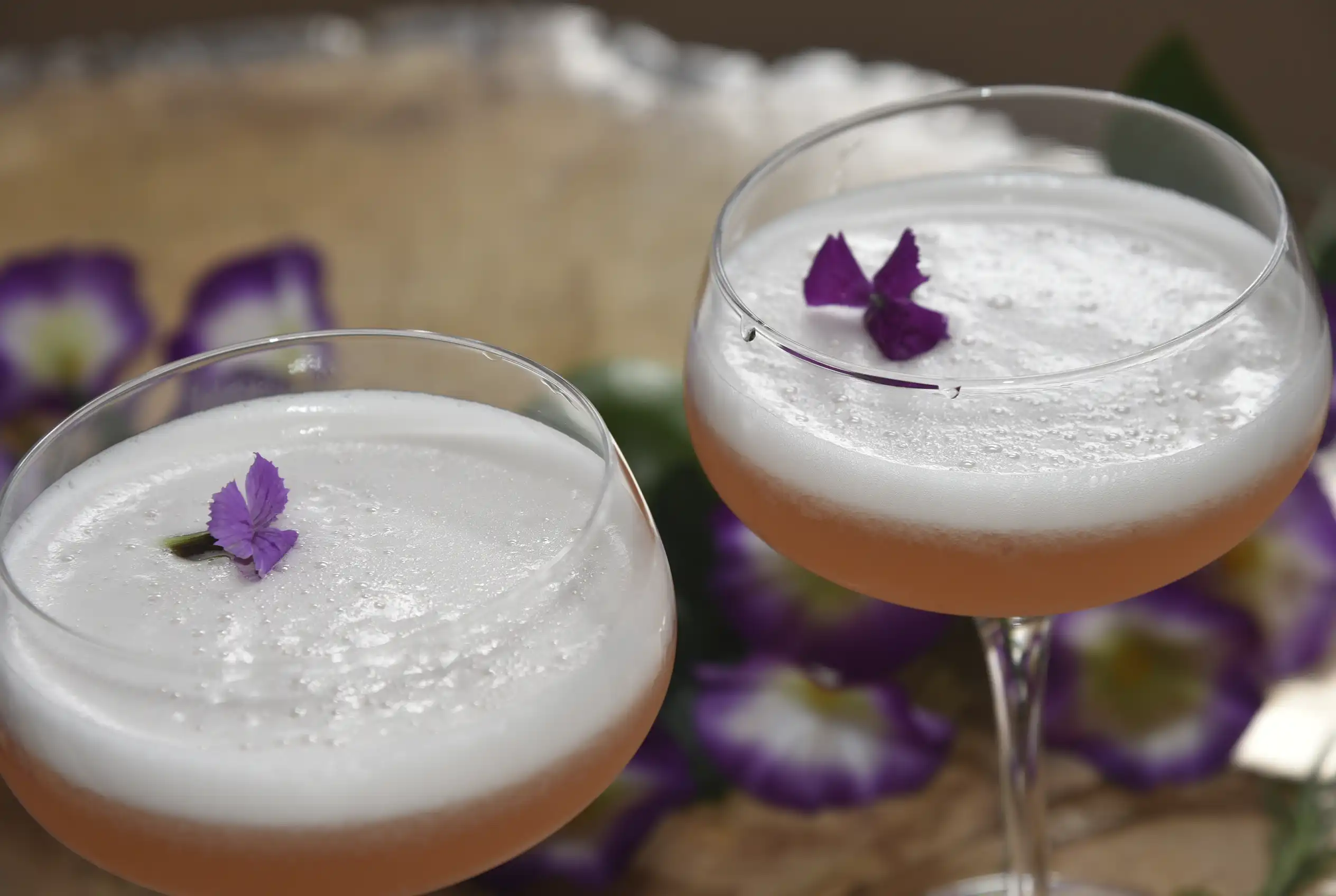 Dos copas de Pisco Sour con espuma cremosa y flores púrpuras comestibles, servidos en la barra del Restaurante 3 Soles.