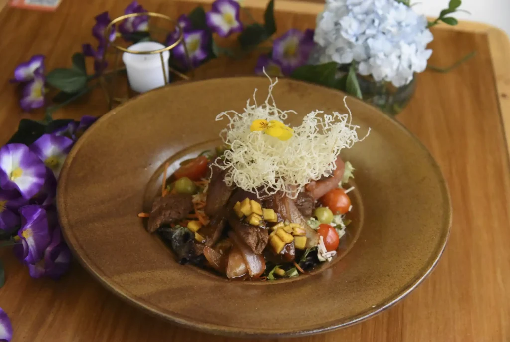 Elegante plato de cocina fusión peruana con lomo, vegetales frescos y nido de arroz crocante, decorado con flores en el Restaurante 3 Soles.