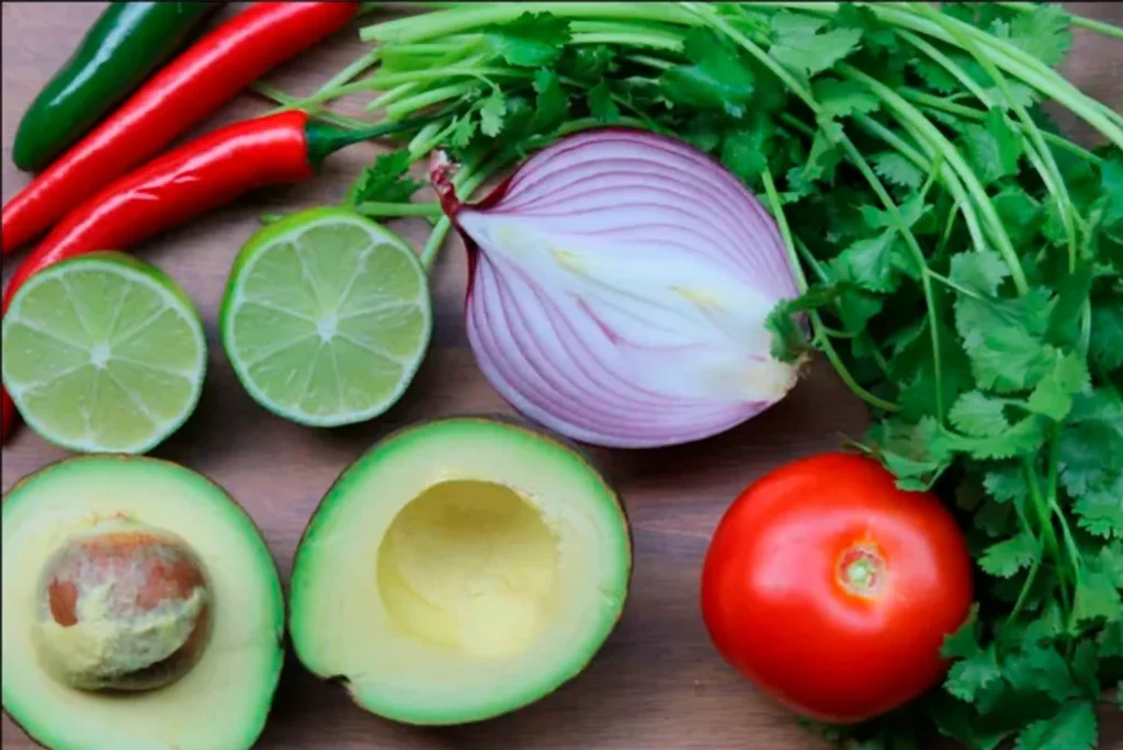 Ingredientes frescos para guacamole: aguacate, tomate, cebolla, limón y cilantro sobre tabla de madera.