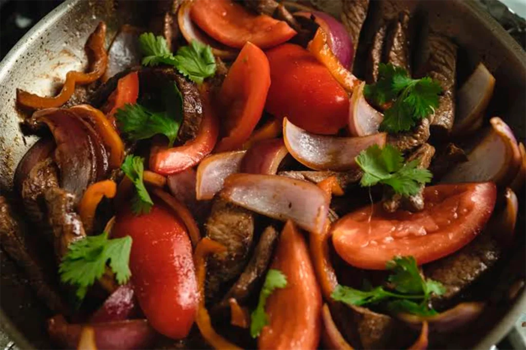 Lomo saltado en sartén con tomate, cebolla morada y cilantro fresco