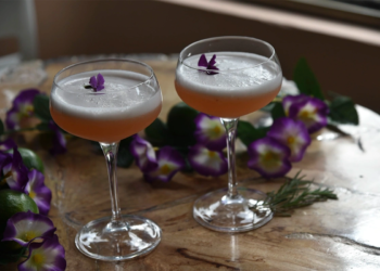 Dos copas de pisco sour con flor comestible y flores decorativas en 3 Soles