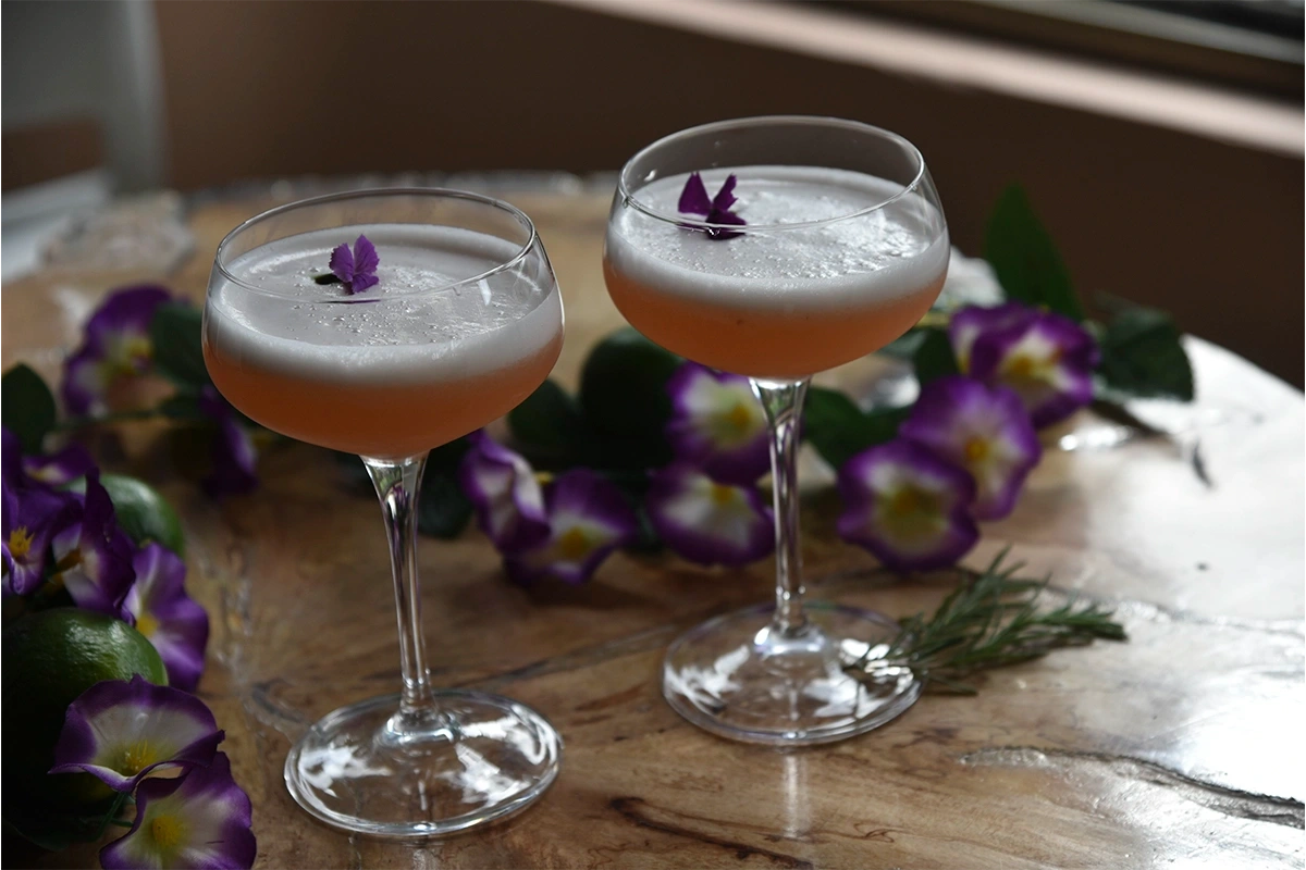 Dos copas de pisco sour con flor comestible y flores decorativas en 3 Soles
