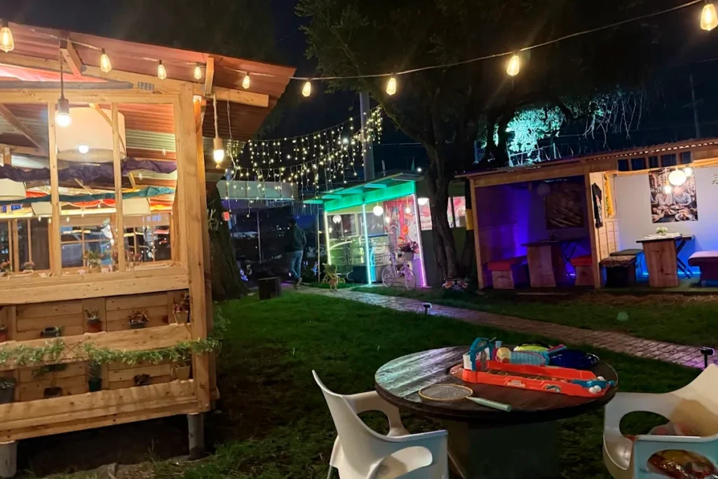 Zona exterior de 3 Soles de noche con luces, cabañas y juegos en Chía