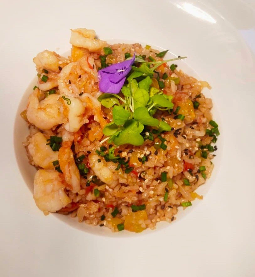 Plato de arroz chaufa de camarón decorado con flores comestibles y ajonjolí.
