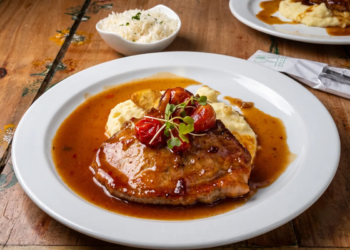 Plato de bondiola de cerdo en salsa de curuba con puré de papa servido sobre mesa de madera.