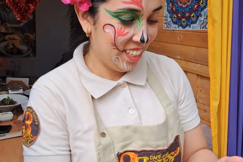 Smiling waitress with catrina face paint and a flower in her hair during day of the dead celebration.