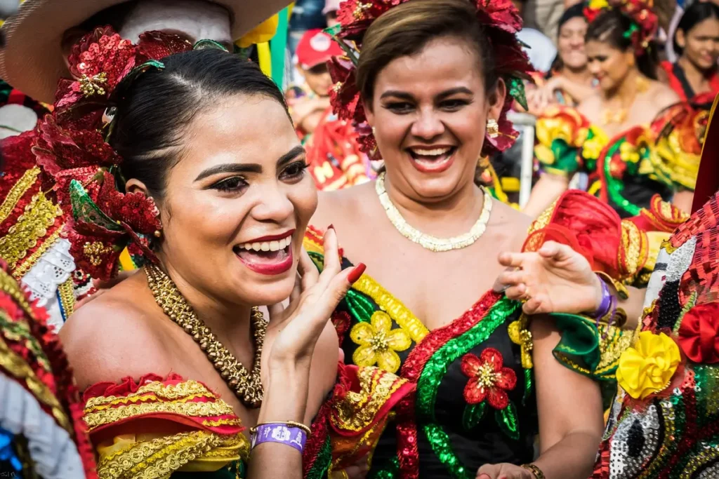 Two women smiling in traditional parade dresses during a cultural festival celebration.