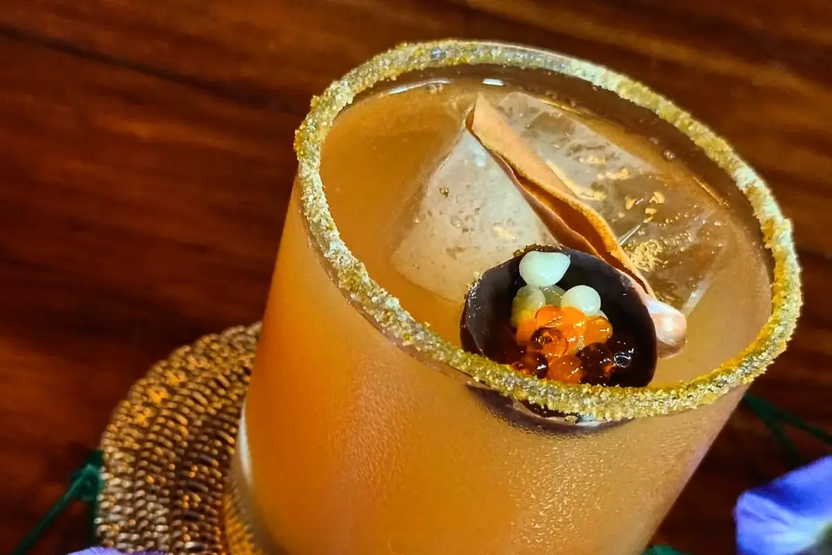 Craft autor cóctel topped with molecular gastronomy pearls and a sugar rim on a wooden table.