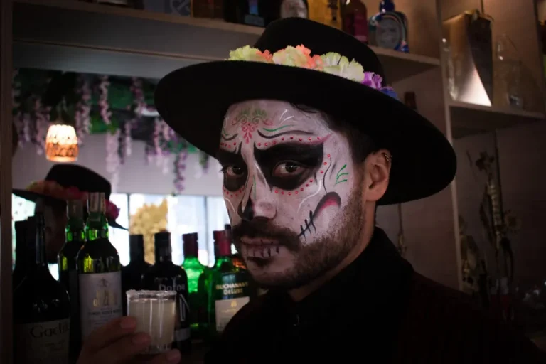 Man dressed as catrin holding a shot glass at a restaurant bar during halloween in chia.