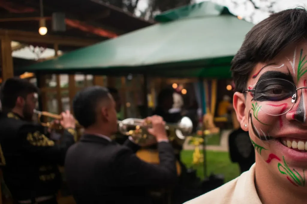 Young man smiling with themed face paint at an outdoor event with a live mariachi band performing in chia.