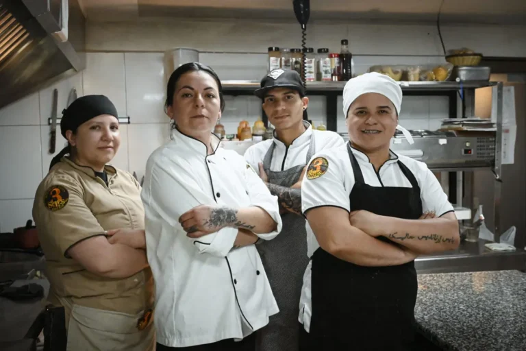 Four kitchen staff members and chefs posing with crossed arms inside a restaurant kitchen.